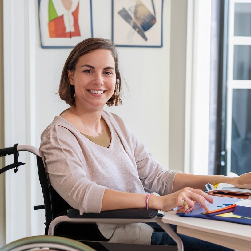 Photo of a smiling woman in a wheelchair in front of a desk at home